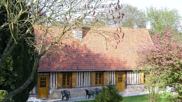 Un edificio tradizionale con tetto in tegole, fondamenta in pietra e porta in legno. Sono presenti tavoli e sedie all'aperto, e un prato curato.