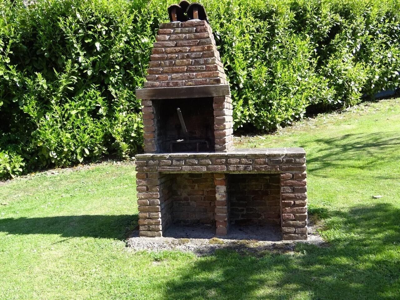 Forno de tijolos ao ar livre com chaminé, cercado por grama e sebes.
