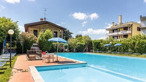 A swimming pool with sun loungers, a covered seating area, and adjacent buildings. - Apartment 'Casa Cattaleya' with Shared Pool, Private Terrace and Shared Garden (Desenzano del Garda)