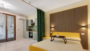 A modern bedroom with a bed, bedside table, and a view of a kitchen. - Apartment 'Casa Cattaleya' with Shared Pool, Private Terrace and Shared Garden (Desenzano del Garda)