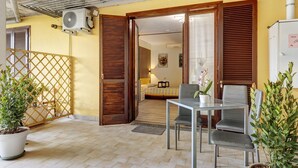 A room with a bed, a table, chairs, a potted plant, and a window with blinds. - Apartment 'Casa Cattaleya' with Shared Pool, Private Terrace and Shared Garden (Desenzano del Garda)