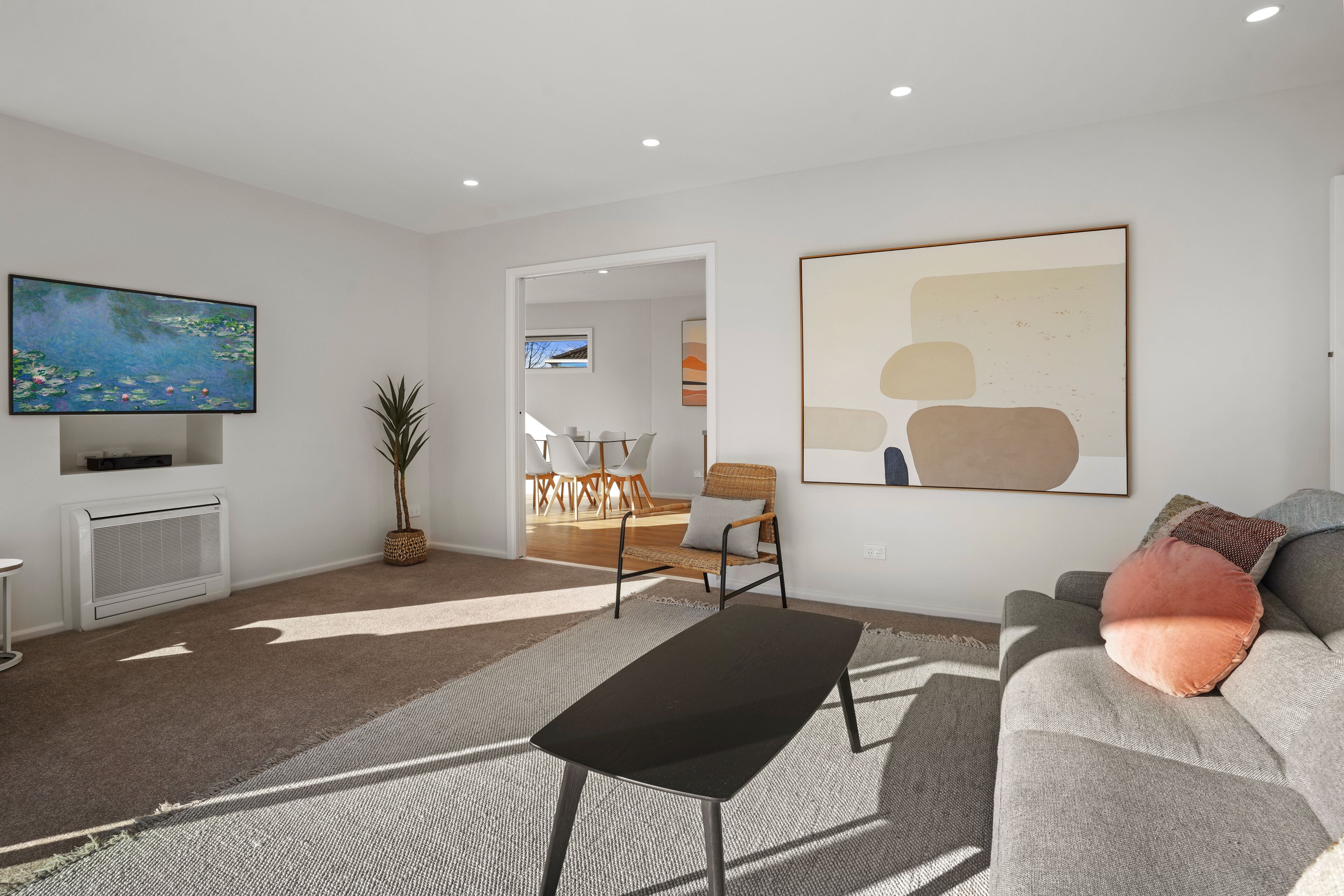 A modern living room with a flat-screen TV, a grey sofa, a black coffee table, and a large abstract painting.