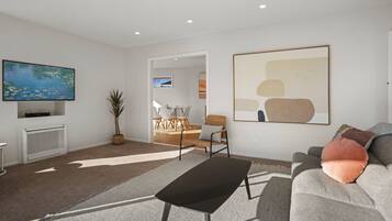 A modern living room with a flat-screen TV, a grey sofa, a black coffee table, and a large abstract painting.