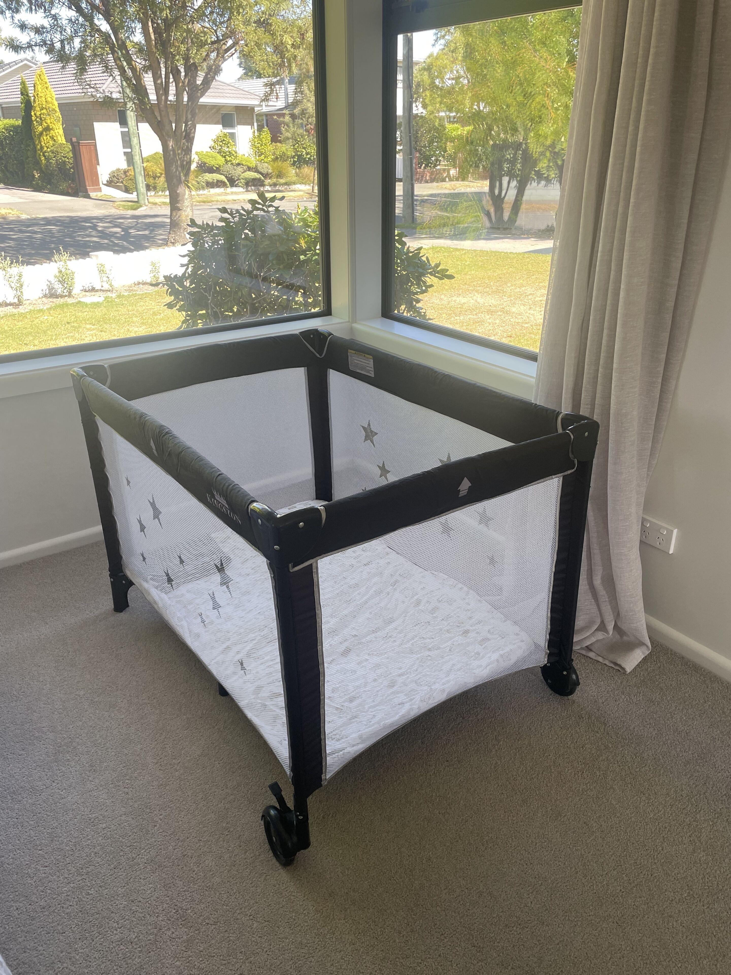 Um cercado infantil com rodinhas em um quarto com janelas amplas.