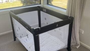 Um cercado infantil com rodinhas em um quarto com janelas amplas.