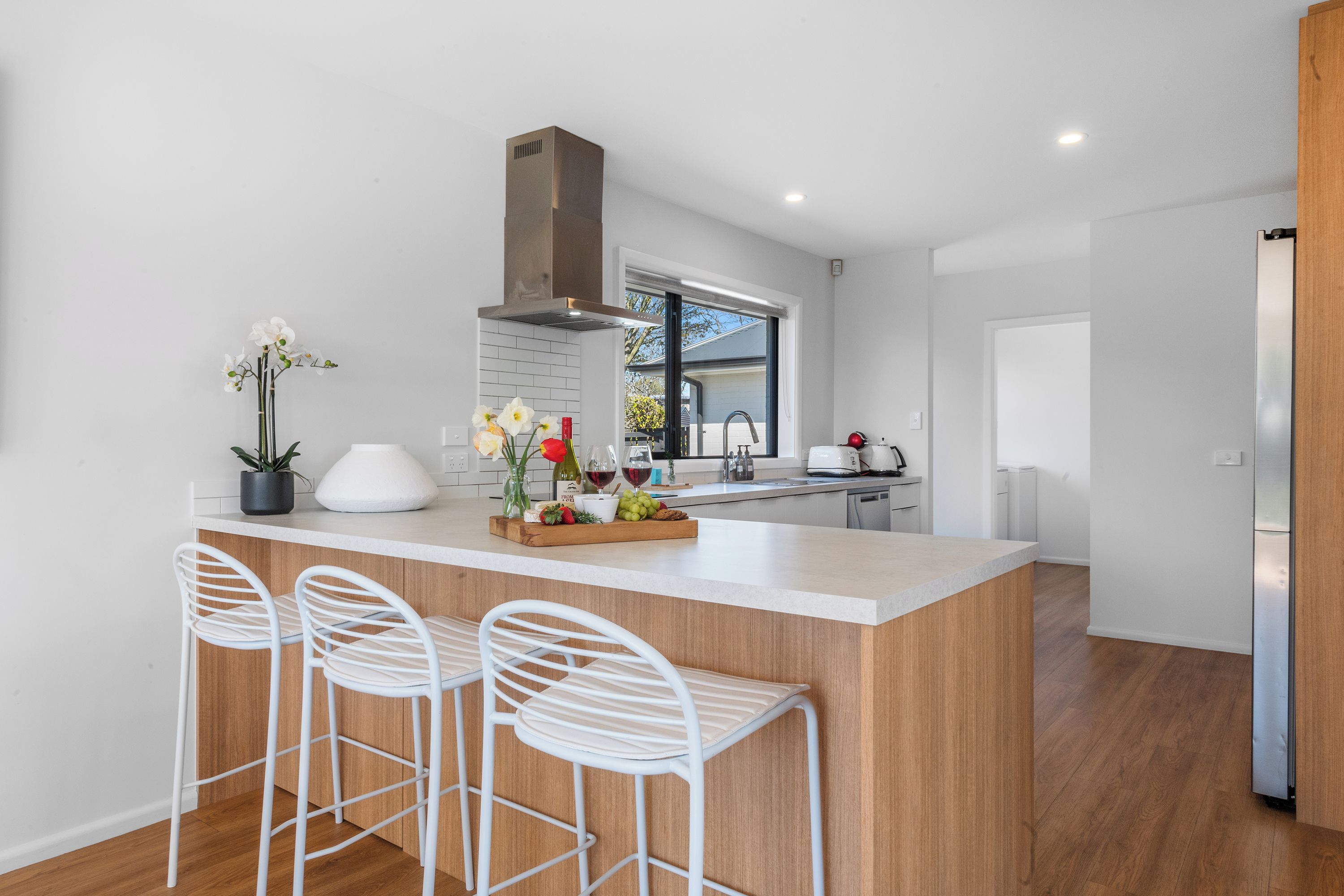 A modern kitchen with a central island, bar stools, a window, and a built-in oven.