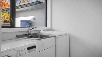 Uma área de lavanderia moderna com uma máquina de lavar Bosch, uma pia e uma janela com vista para árvores.