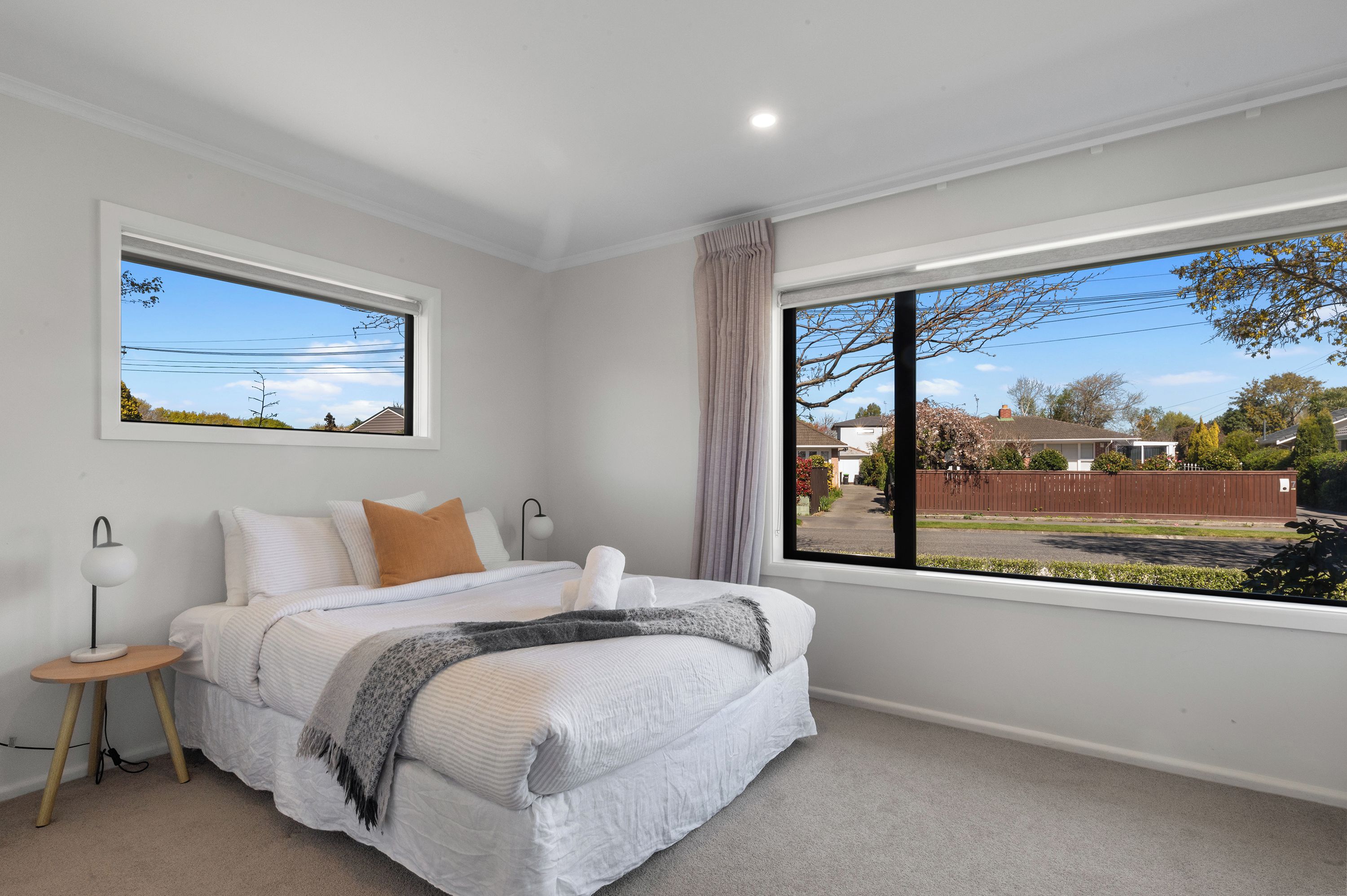 A bedroom with a bed, a bedside table, a lamp, a window with a view of the outside, and a curtain.