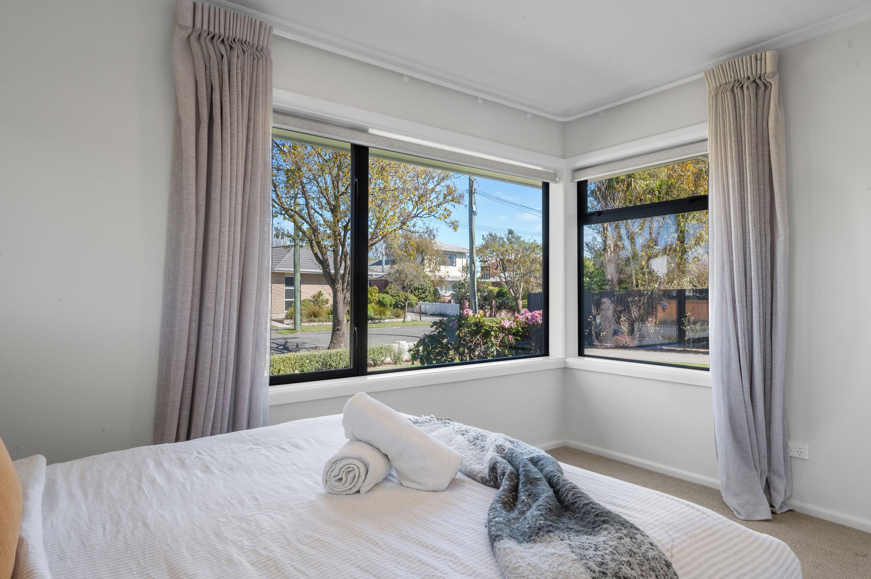 Un dormitorio con cama, dos ventanas y cortinas.