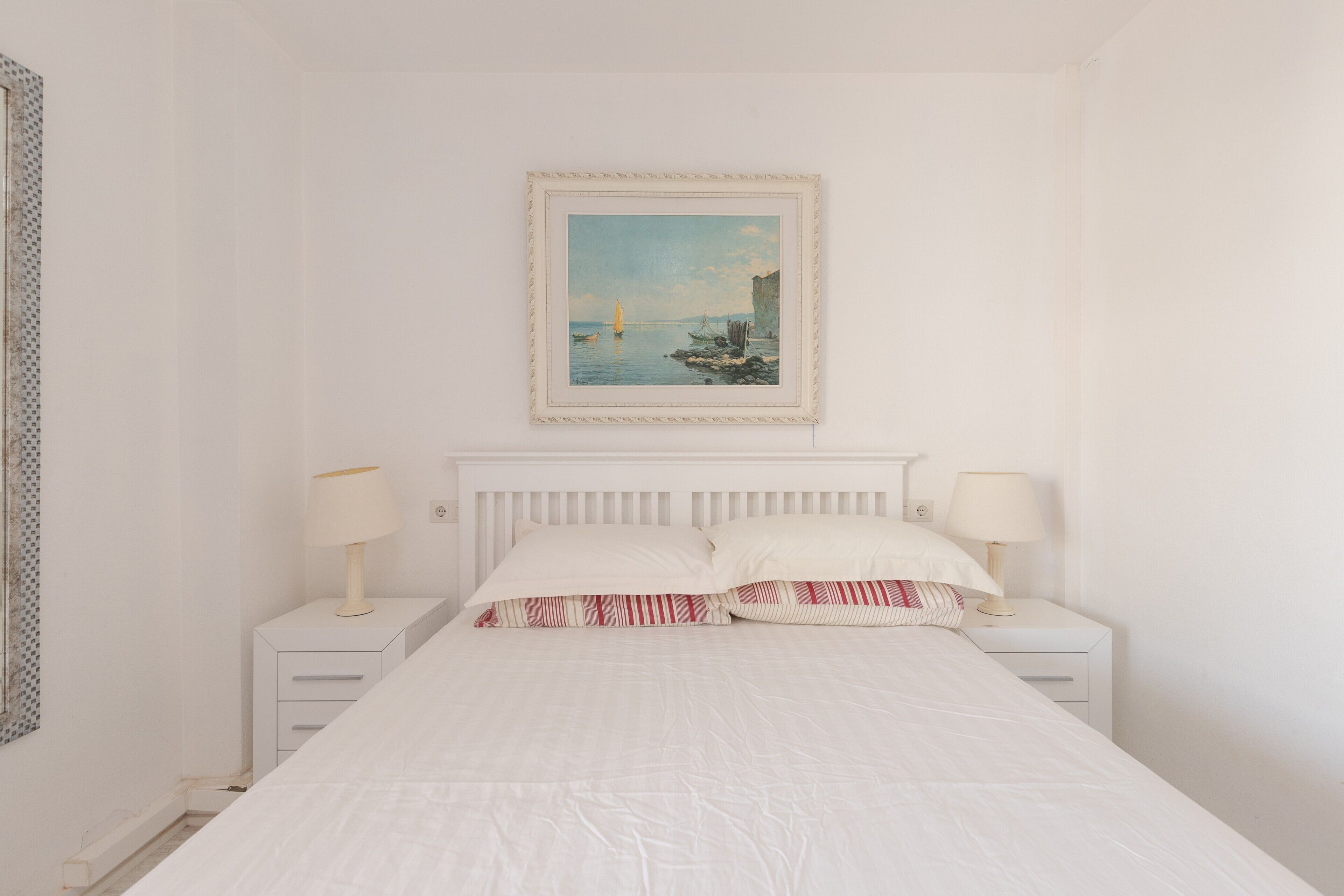 A bedroom with a bed, two bedside tables, a nightstand, a framed painting, and a window.