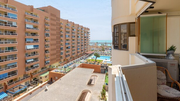A high-rise hotel with multiple balconies, a rooftop pool, and a view of the sea.