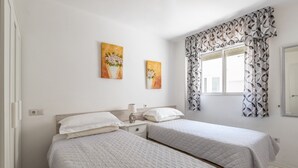 A bedroom with two beds, a window with patterned curtains, and two wall-mounted paintings.