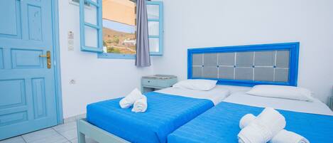 A room with two beds, a window with a view, a blue door, and a blue headboard.