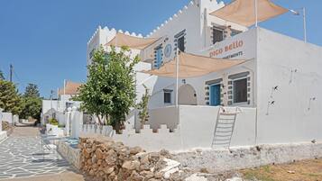 A white building with a sign reading 'DICO BELLO APARTMENTS' and a stone wall in the foreground.