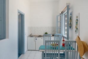 Cocina compacta con comedor, que incluye un refrigerador blanco, un lavamanos y una mesa con sillas.