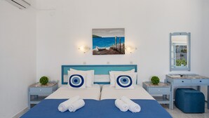 Une chambre d’hôtel avec un lit, un bureau, une chaise, une petite plante et un tableau représentant une scène de plage.