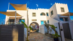 Un bâtiment blanc avec une enseigne indiquant « Pico Bello », une entrée fermée par un portail et une cour dallée de pierres.