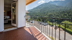 Un balcon donnant sur une chaîne de montagnes boisées, une zone pavée et l’entrée d’un bâtiment.