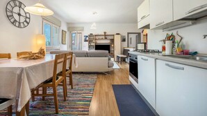 Une cuisine moderne avec des meubles blancs, un coin repas avec une table et des chaises, et un salon avec un canapé et une cheminée.
