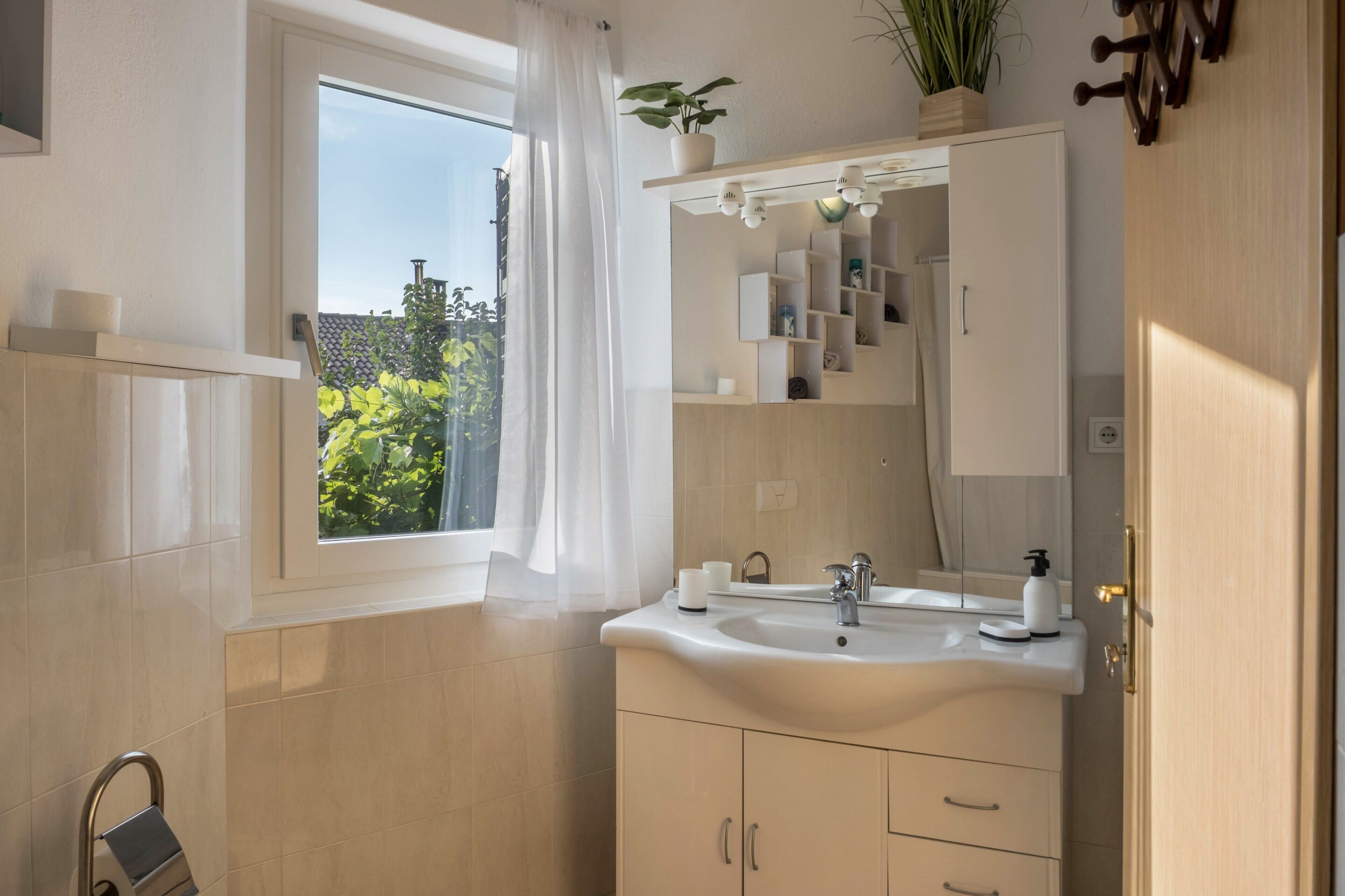 Ein Badezimmer mit Fenster, Waschbecken, Spiegel und Schrank.