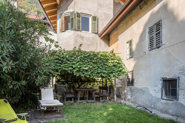 A courtyard with a table and chairs, surrounded by buildings with shutters.