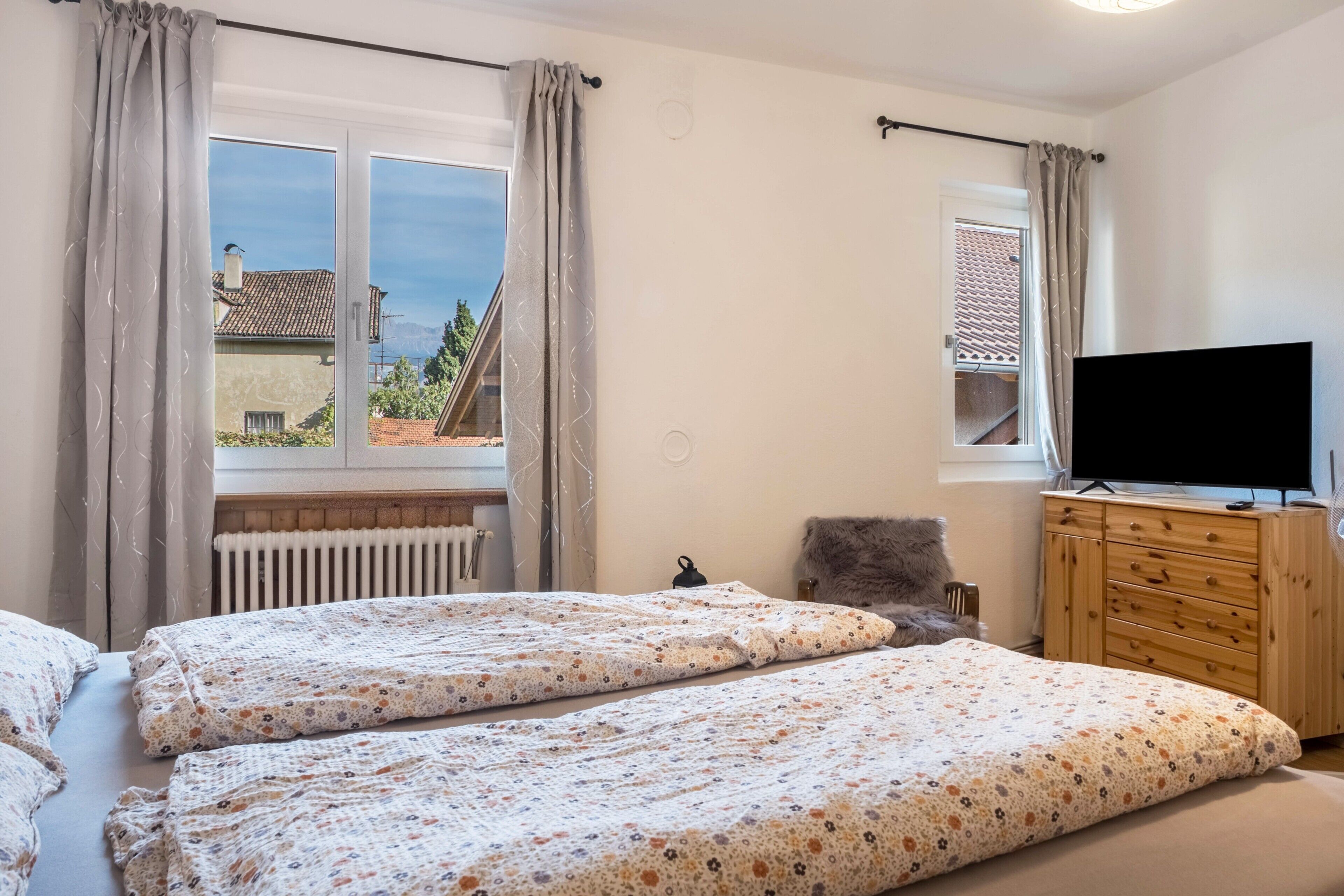 A bedroom with two beds, a TV, a wooden dresser, and a window with curtains.