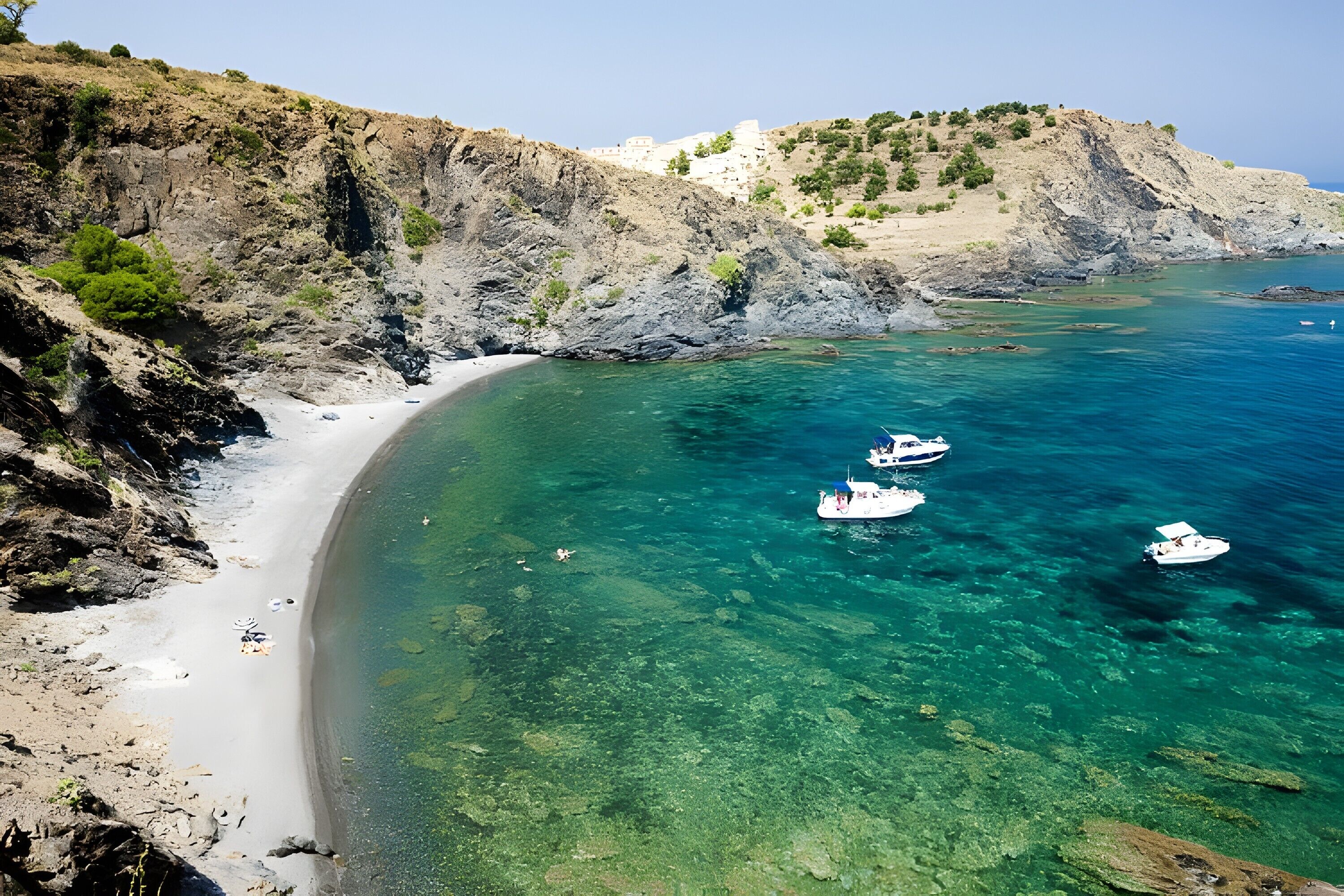 Eine Küstenlandschaft mit klarem türkisblauem Wasser, felsigen Klippen und einem Sandstrand.