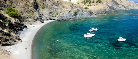 Et kystområde med klart turkis vand, klipper og en sandstrand.