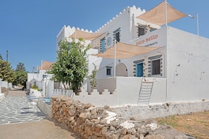 Un edificio blanco con balcones, un muro de piedra y un cielo despejado.