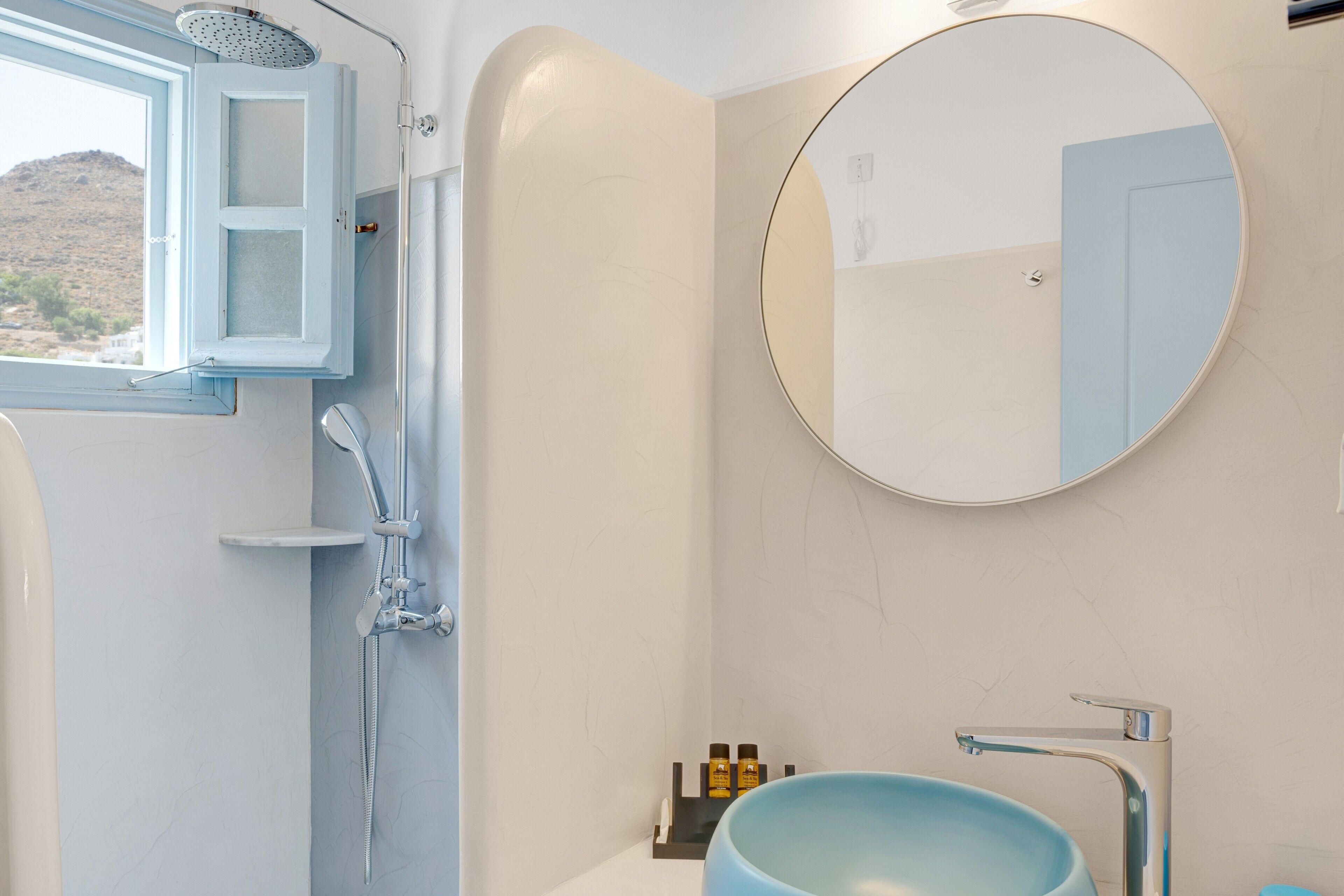 Een badkamer met een douche, wastafel, spiegel en een raam.