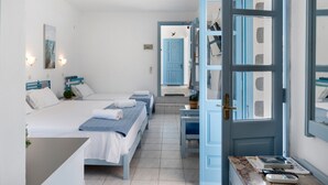 Hotellihuone, jossa on kolme sänkyä, työpöytä, tuoli, ikkuna, josta on näkymä, ja ovi, joka johtaa toiseen huoneeseen.