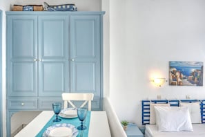 Una habitación con un armario azul grande, una mesa de comedor con cristalería azul, una silla blanca y una cama con cabecera azul y almohadas blancas.