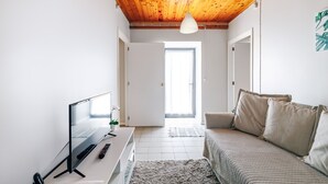 Et moderne værelse med træloft, et skrivebord med en computer, en seng med beige sengetøj og et stort vindue.