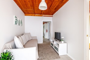A living room with a wooden ceiling, a white sofa, a TV on a white stand, and a plant.