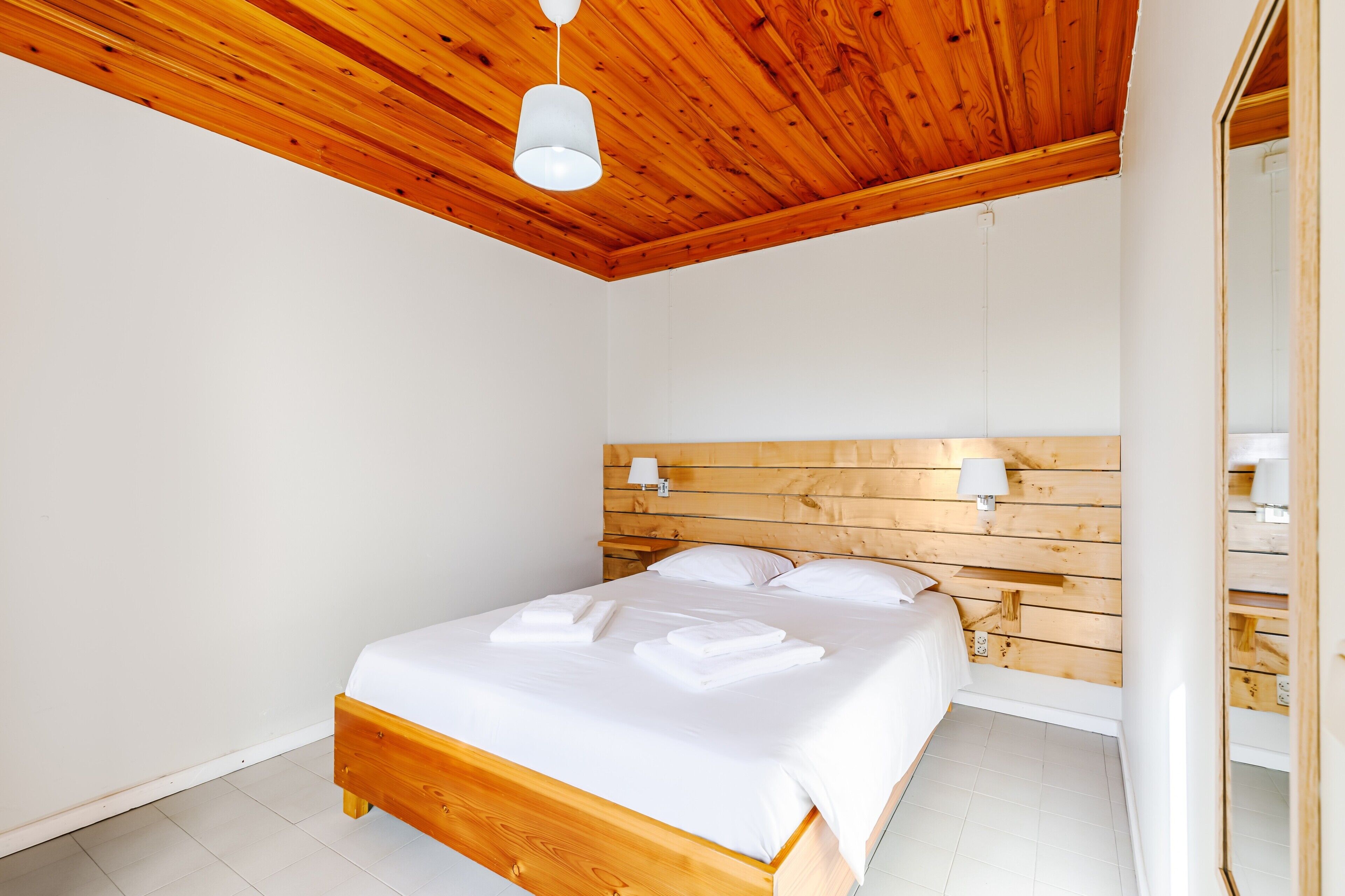 Un dormitorio con cabecera de madera, cama con ropa de cama blanca y dos lámparas de noche.