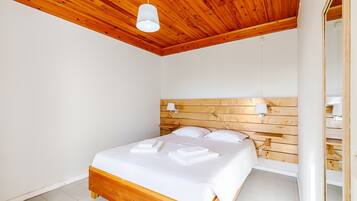 Un dormitorio con cabecera de madera, cama con ropa de cama blanca y dos lámparas de noche.