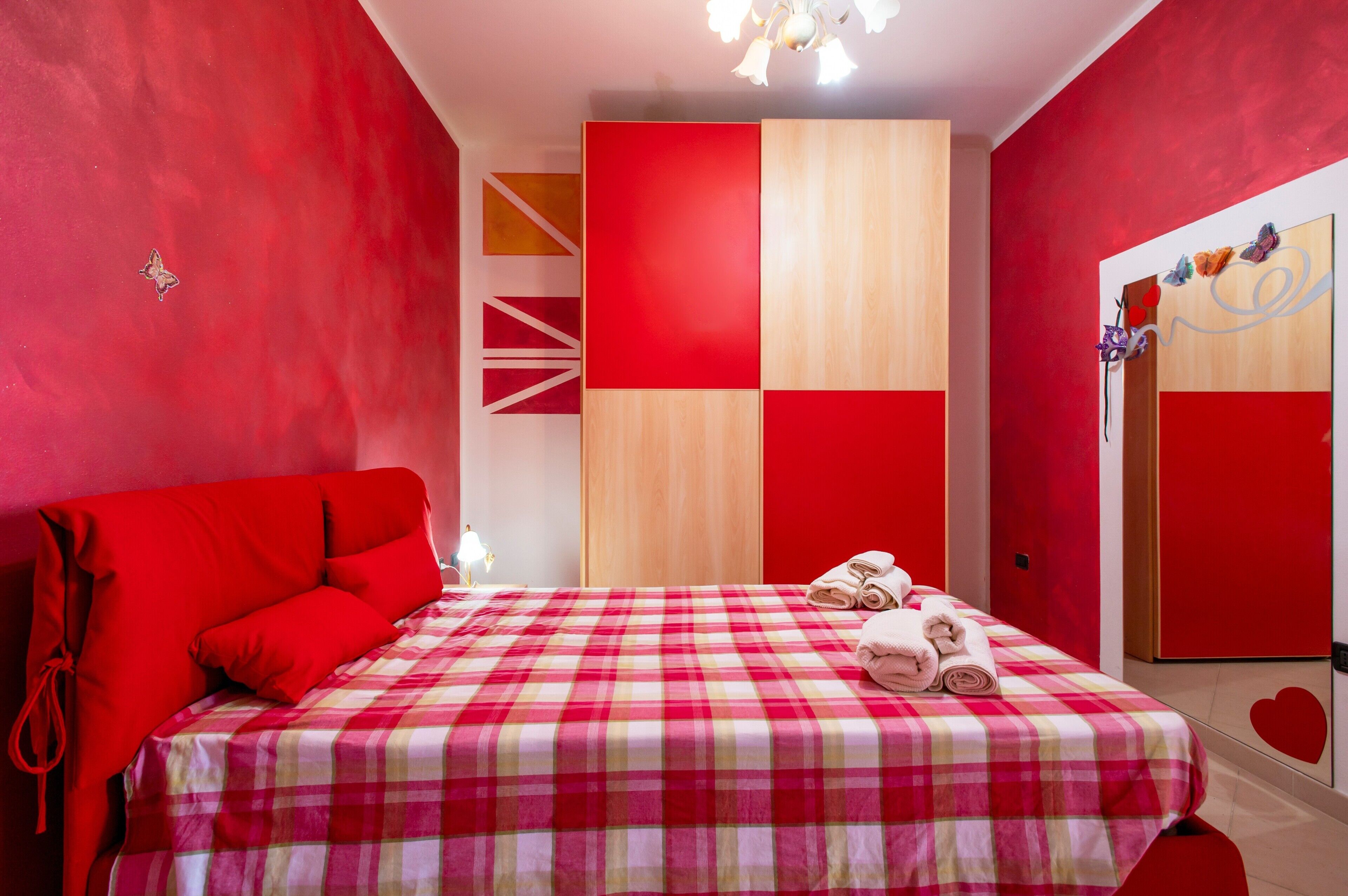 Une chambre d’hôtel avec une couvre-lit à carreaux rouges et blancs, un canapé rouge et un mur recouvert de panneaux de bois.