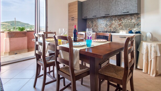 Un coin repas avec une table dressée pour quatre personnes, une cuisine dotée de meubles modernes et une vue sur les collines.