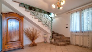 Un escalier avec une rampe verte, une armoire en bois, un vase contenant des plantes séchées et un tapis à motifs.