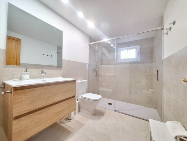 A modern bathroom with a wooden vanity, a glass shower enclosure, and a white toilet.