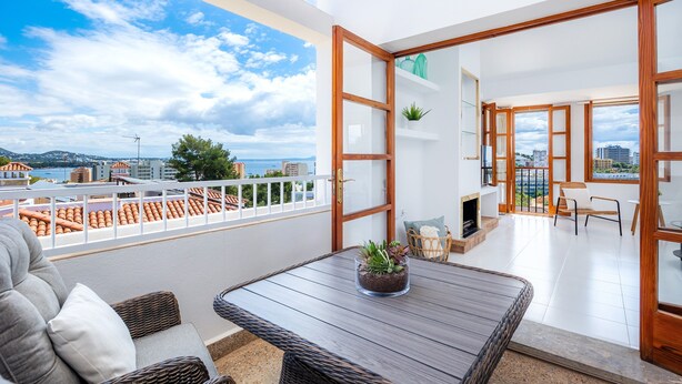 A balcony with a view of the city, a table with a plant, wicker furniture, and a door leading to an interior space. - Holiday Home 'Ca Na Luisa' with Sea View, Wi-Fi and Air Conditioning (Palmanova)
