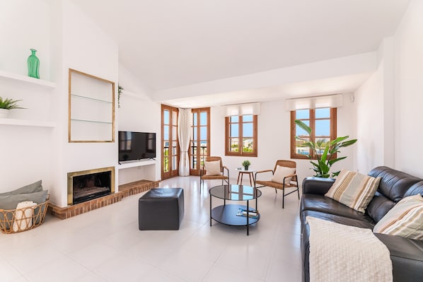 A spacious living room with a fireplace, a black leather sofa, a round coffee table, and a television.