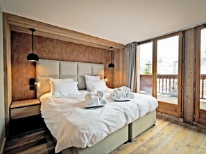 A spacious bedroom with a large bed, two bedside tables, and a view of a wooden deck through a sliding glass door. - Family chalet for 12 with jacuzzi and ski-in/ski-out (Les Menuires)