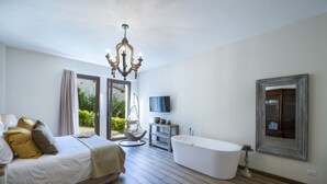 Un dormitorio con una cama, una silla colgante, un televisor, una bañera y un espejo grande.