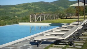 Zona junto a la piscina con sillones de descanso y vistas a un paisaje montañoso.