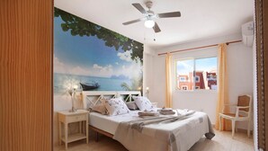 A bedroom with a bed, a ceiling fan, a nightstand, a chair, a window with curtains, and a mural of a beach scene. - Vacation Home 'Little Dunes' with Shared Pool, Terrace & Wi-Fi (Corralejo)