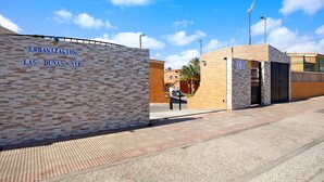 A building entrance with a sign reading 'URBANIZACION LAS DUNAS N19' and a gated entrance. - Vacation Home 'Little Dunes' with Shared Pool, Terrace & Wi-Fi (Corralejo)