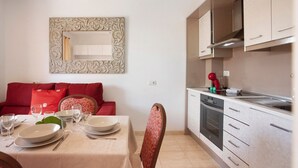 A dining area with a table set for four, a red sofa, and a kitchen with white cabinets and a red kettle. - Vacation Home 'Little Dunes' with Shared Pool, Terrace & Wi-Fi (Corralejo)