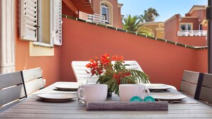 A dining table with chairs, a vase with flowers, and a view of a building with balconies. - Vacation Home 'Little Dunes' with Shared Pool, Terrace & Wi-Fi (Corralejo)