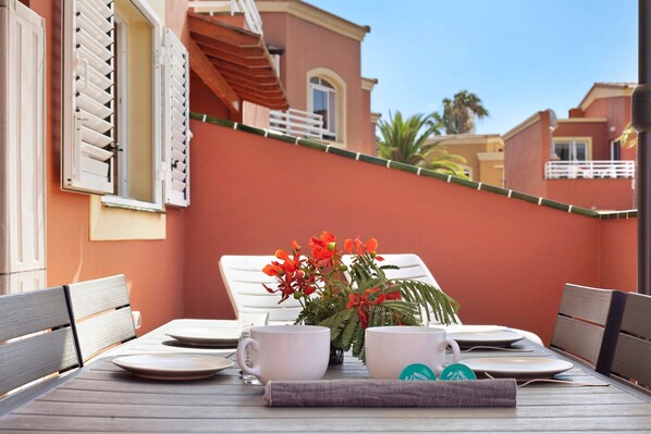 A dining table with chairs, a vase with flowers, and a view of a building with balconies.
